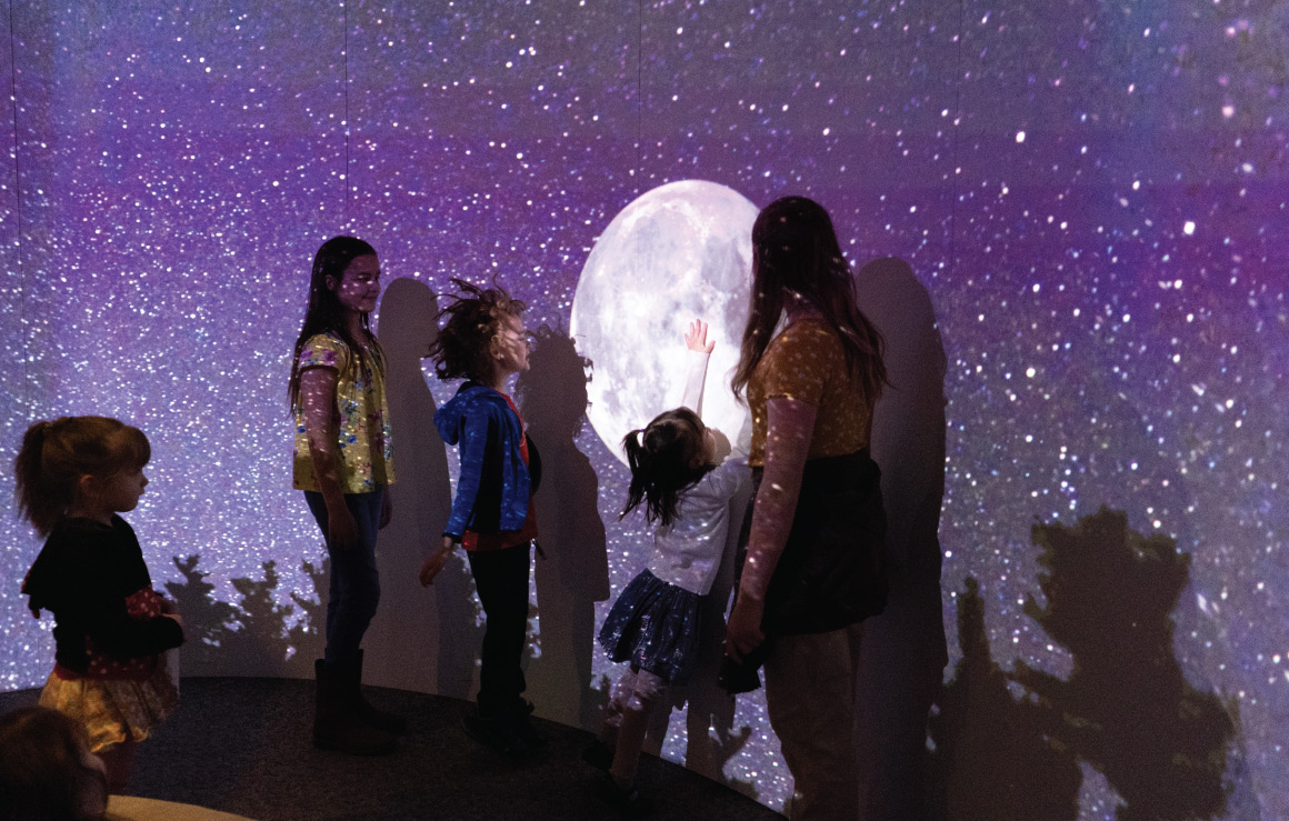 Des enfants interagissent avec une projection murale de la Lune et des étoiles.