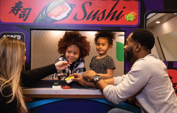 Deux enfants dans un mini-camion casse-croûte servent du sushi jouet à deux adultes.