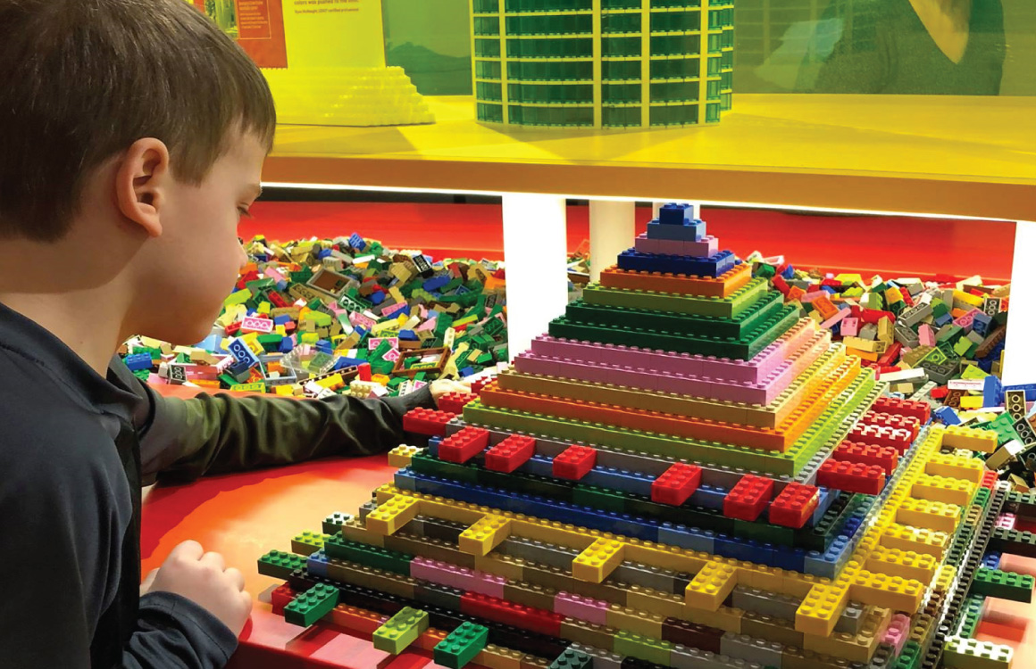 Un garçon construit une structure pyramidale en Lego.