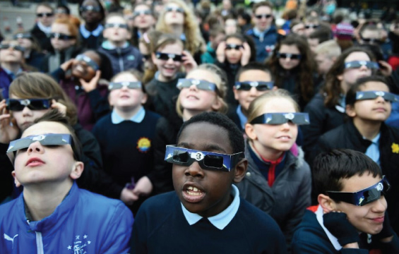 Un groupe d'élèves regardent le ciel, munis de lunettes pour éclipse.