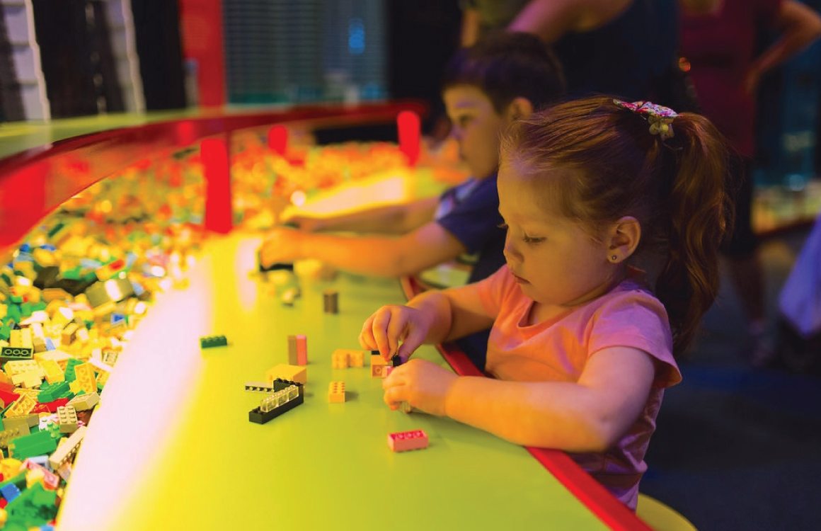 De petits enfants construisent avec des briques Lego à une table.” width=