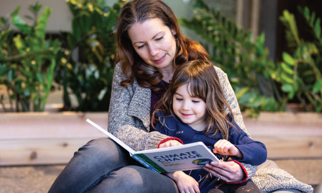 Une femme lit un livre appelé «Climate Change», une enfant assise sur ses genoux.