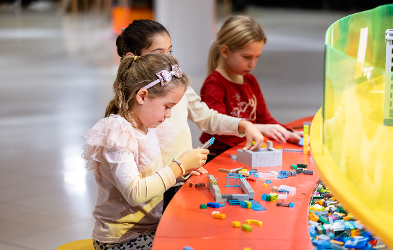 Trois filles à une table d'exposition jouent aux Lego.