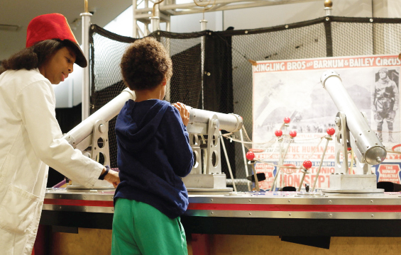 Une animatrice du Centre des sciences et un enfant interagissent avec un module de l'exposition Le Cirque! La science sous le chapiteau.